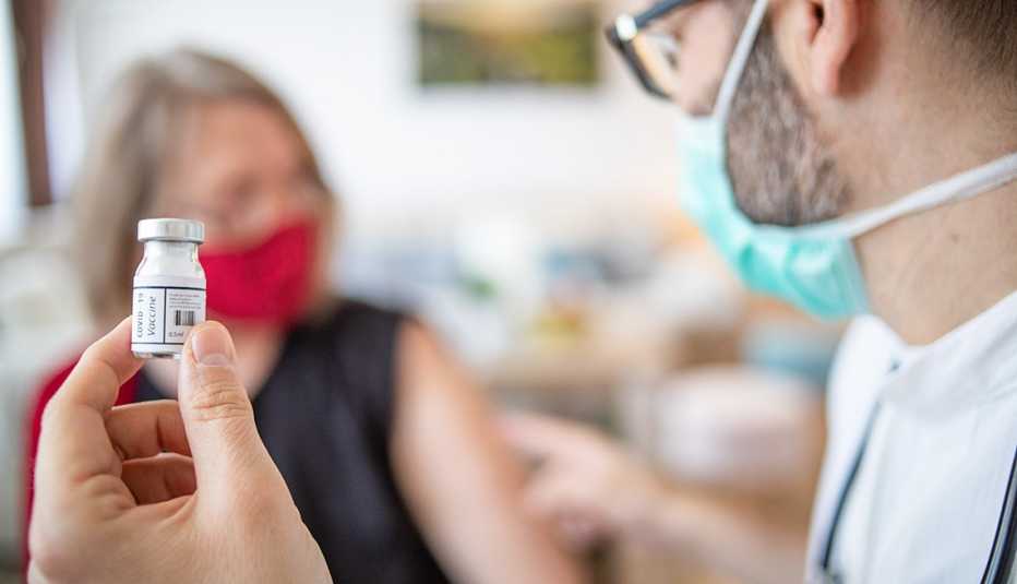 Un médico sostiene un vial mientras señala el brazo de una paciente.
