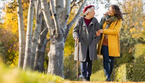 Two women walk through a park on an autumn day.