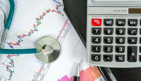 Primer plano de una calculadora con facturas médicas y un estetoscopio.