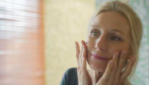 Mujer toca su rostro mientras examina sus ojos