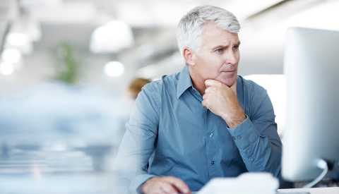 Hombre mayor sentado frente a una pantalla de computador - Cómo enfrentar la pérdida auditiva en el lugar de trabajo