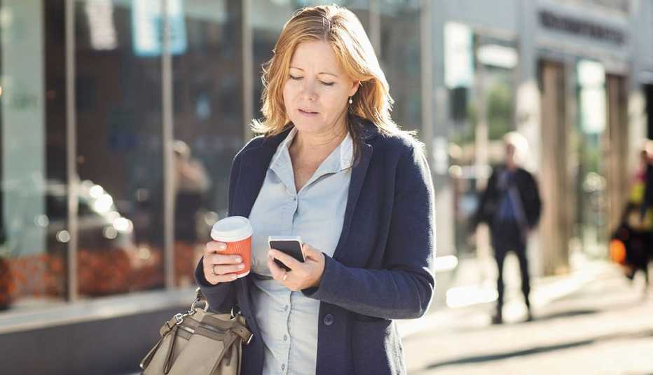 Mujer mirando su celular mientras camina por la calle Mujer mirando su celular mientras camina por la calle
