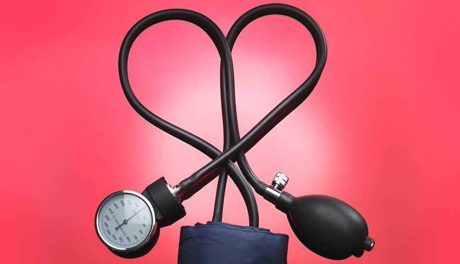 El cordón de un aparato para medir la presión forma un corazón sobre un fondo rojo El cordón de un aparato para medir la presión forma un corazón sobre un fondo rojo