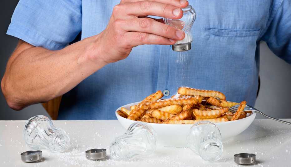 Persona poniéndole sal a sus papas fritas