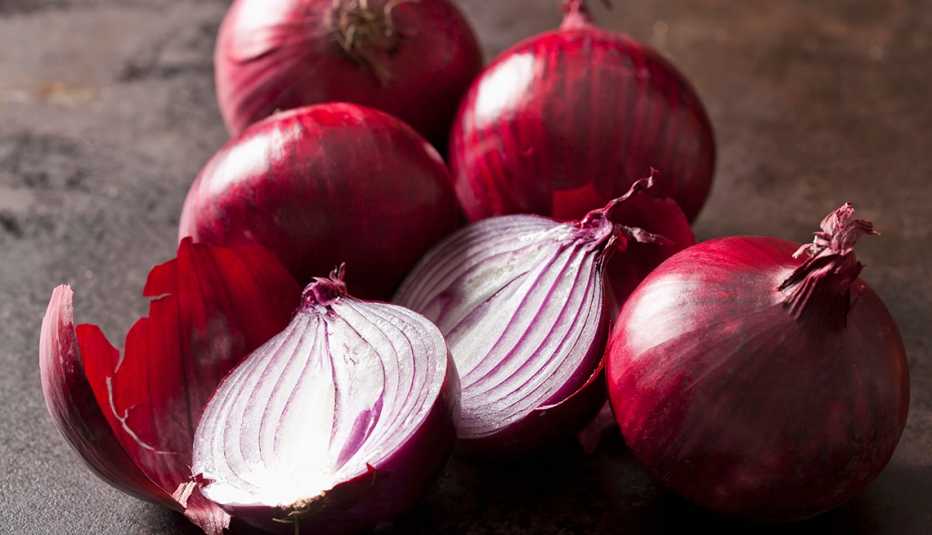 Varias cebollas moradas sobre una mesa, una cortada a la mitad Varias cebollas moradas sobre una mesa, una cortada a la mitad