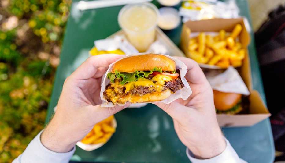 Una persona comiendo una hamburguesa con queso y papas fritas