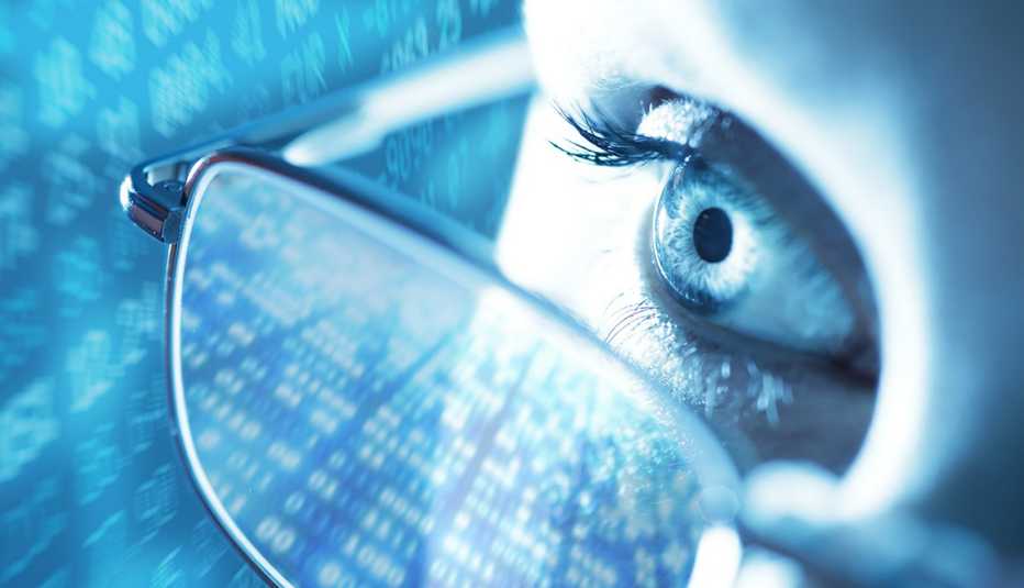 Acercamiento a un ojo de una mujer que usa lentes y una pantalla con datos en el fondo.