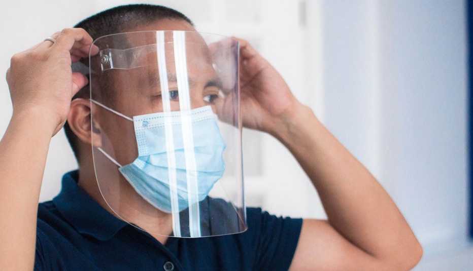 Un hombre se coloca un protector facial y también usa una mascarilla