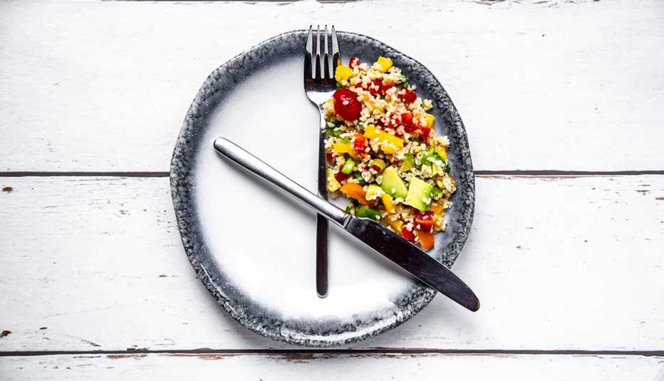 Ensalada en un lado de un plato y los cubiertos simulando un reloj Ensalada en un lado de un plato y los cubiertos simulando un reloj