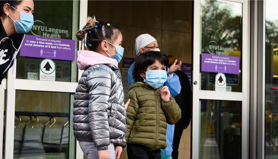 Dos niños con mascarillas frente a la puerta de un hospital