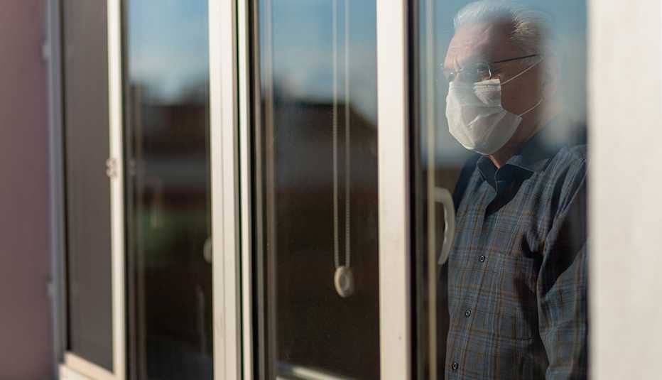 Un hombre con mascarilla mira por una ventana