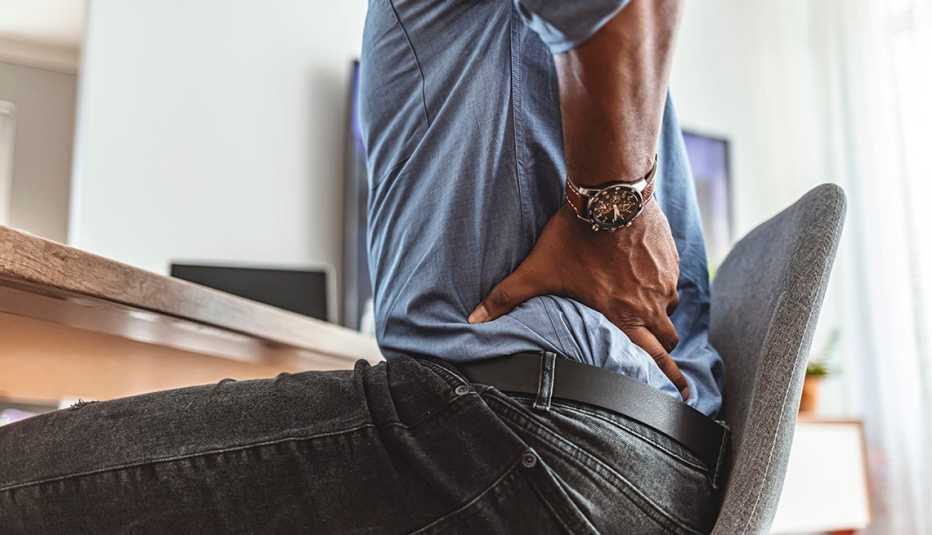 Un hombre sentado se pasa la mano por la espalda baja