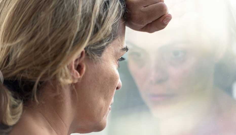 Una mujer, que luce deprimida, mira por una ventana Una mujer, que luce deprimida, mira por una ventana