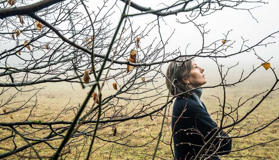 Mujer afuera cerca de un árbol en un día sombrío de otoño con cara de tristeza Mujer afuera cerca de un árbol en un día sombrío de otoño con cara de tristeza