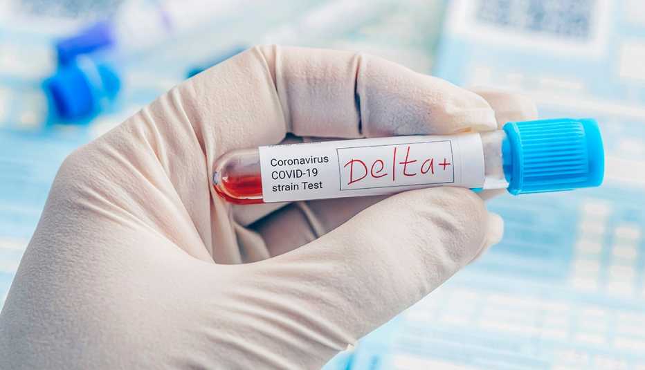 Una mano con guantes sostiene un tubo de ensayo que dice Delta+ Una mano con guantes sostiene un tubo de ensayo que dice Delta+