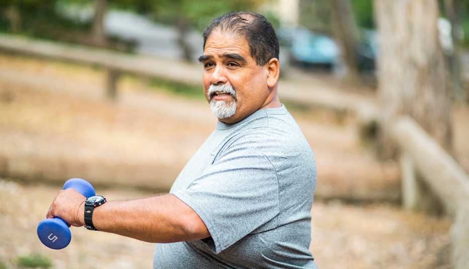 Un hombre se ejercita al aire libre sosteniendo pesas de mano.
