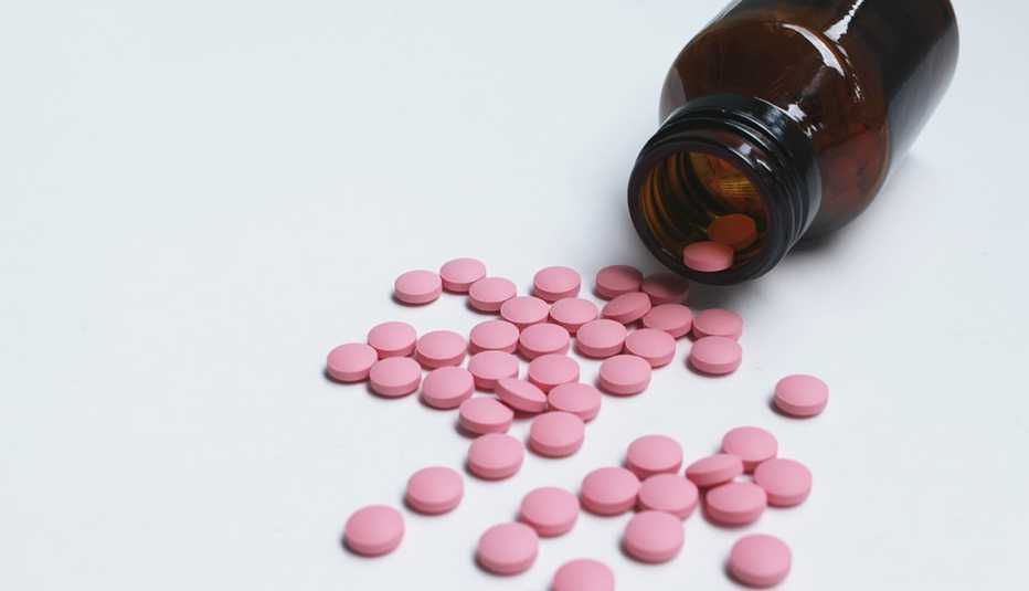 Pastillas rosadas y circulares derramadas sobre una mesa blanca