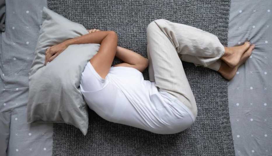 Una mujer en su cama, en posición fetal y con la almohada sobre la cabeza, sin poder dormir Una mujer en su cama, en posición fetal y con la almohada sobre la cabeza, sin poder dormir
