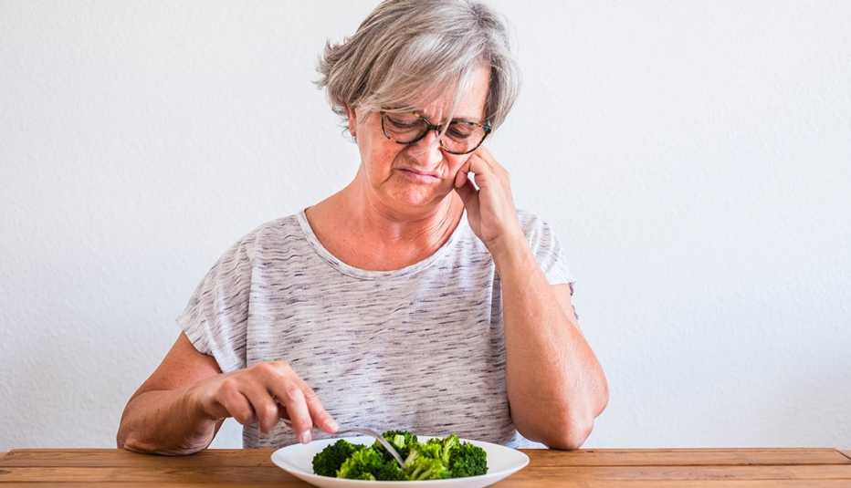 Una mujer mirando con cara de disgusto el brócoli en su plato de comida.