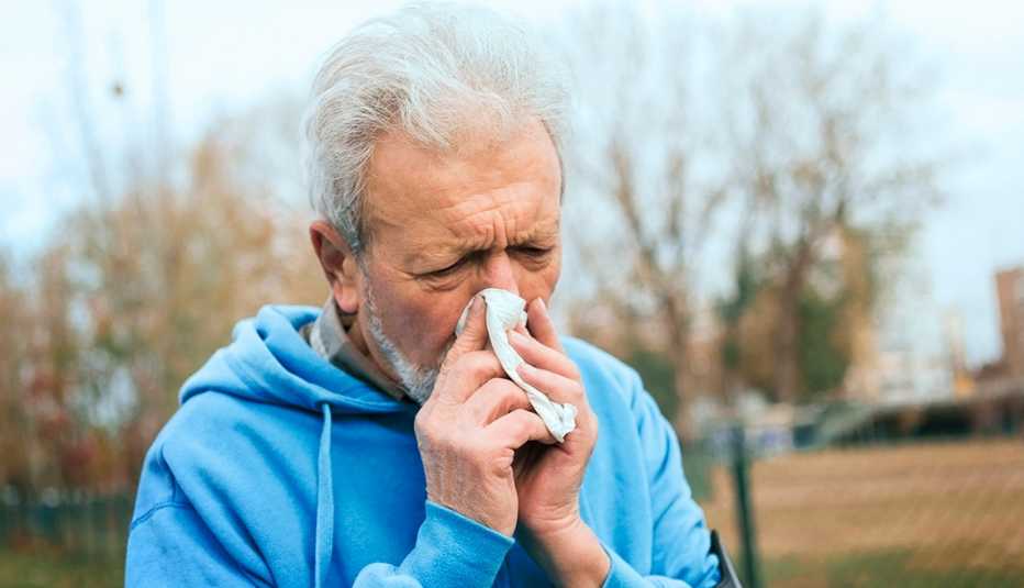 Un hombre con una sudadera con capucha azul se suena la nariz mientras corre por el parque