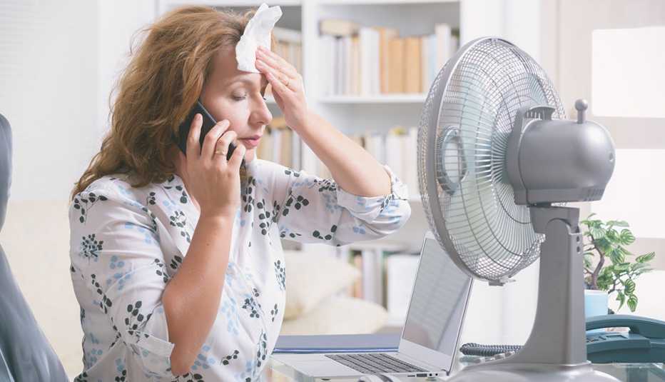 Una mujer habla por teléfono mientras se seca el sudor con un pañuelo sentada frente a un abanico de mesa