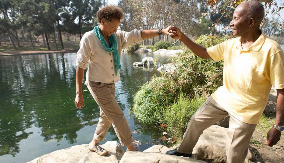 Pareja camina balanceándose sobre unas rocas cerca de un lago
