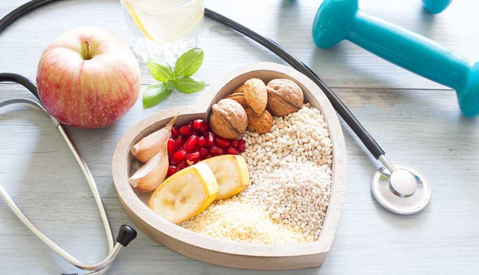 Una manzana, un estetoscopio, unas pesas libres y un plato en forma de corazón con alimentos saludables