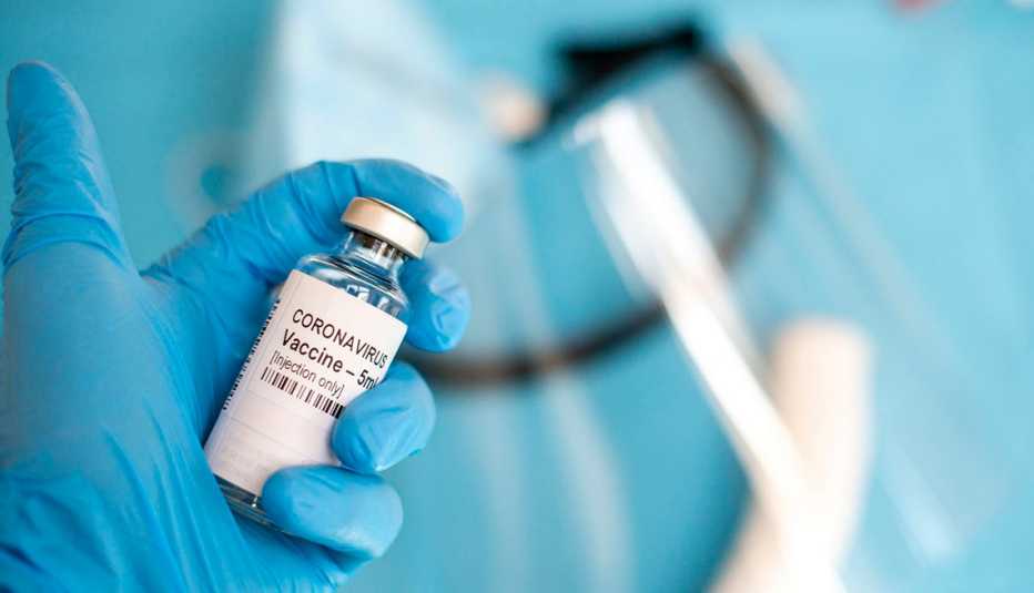Una mano con guante sostiene un frasco de vacuna de coronavirus