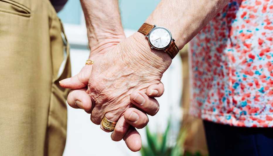 Una pareja de personas mayores tomados de la mano.
