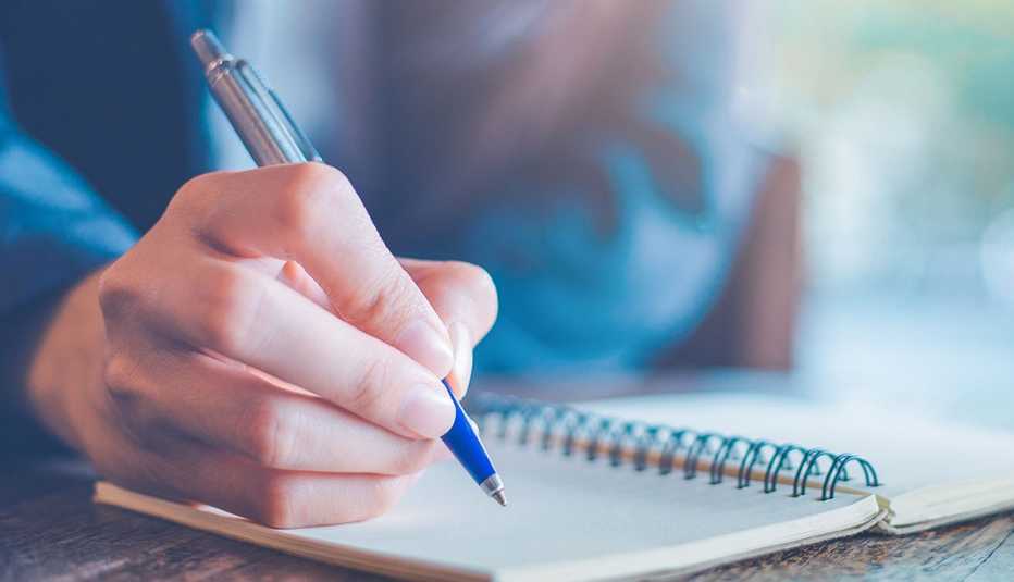 Una persona con un bolígrafo escribiendo en una libreta