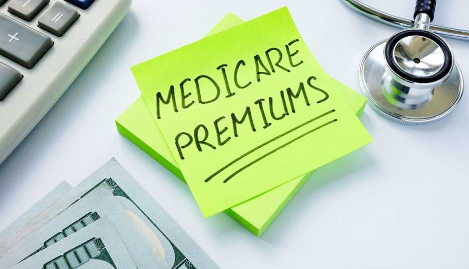 Una nota que dice prima de Medicare sobre un escritorio, tambien se ve un teclado, dinero y un estetoscopio