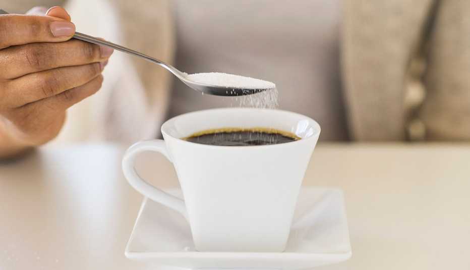 Mujer endulzando su café con azúcar refinada.