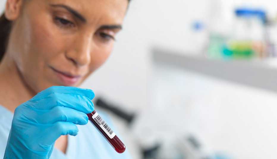 Empleada de un laboratorio observando un tubo de ensayo con una muestra de sangre Empleada de un laboratorio observando un tubo de ensayo con una muestra de sangre