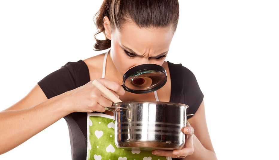 Mujer con una lupa mirando el contenido de una olla