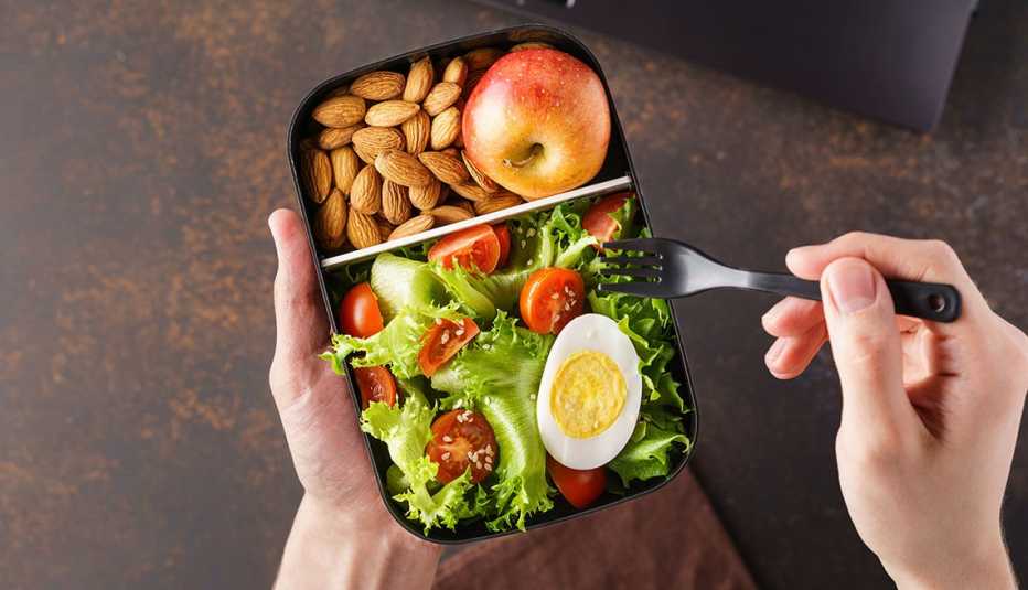 Una persona come ensalada, manzana y almendras