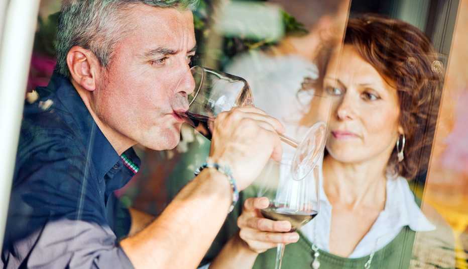 Un hombre maduro toma una copa de vino mientras una mujer lo observa Un hombre maduro toma una copa de vino mientras una mujer lo observa
