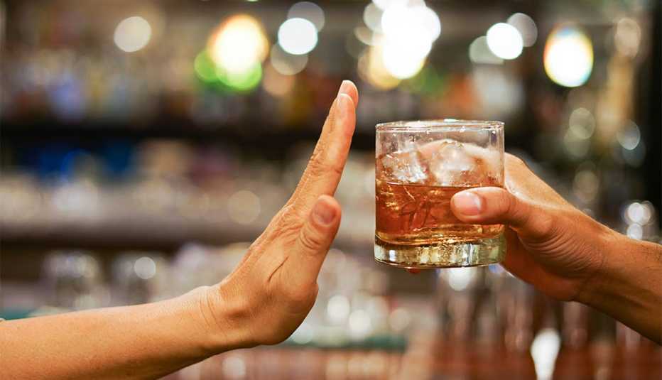 Una mano en señal de detente mientras otra mano le ofrece un vaso con alcohol Una mano en señal de detente mientras otra mano le ofrece un vaso con alcohol
