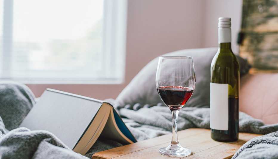 Un libro, una copa de vino y una botella sobre una cama Un libro, una copa de vino y una botella sobre una cama