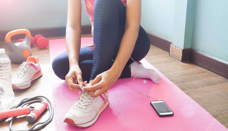Una mujer se amarra las zapatillas de correr y cerca tiene varios aditamentos de ejercicios