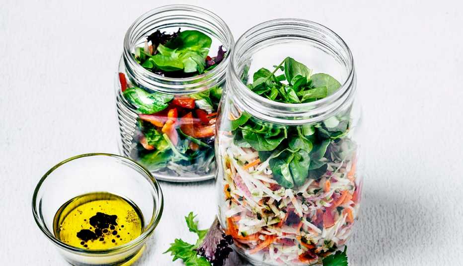 Dos jarras con ensalada y un envase con aderezo de vinagre y aceite