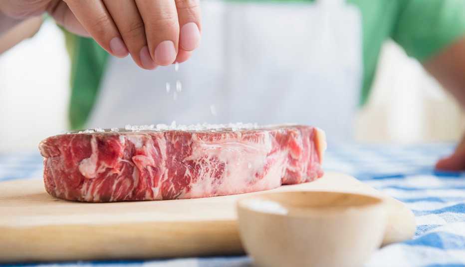 Una persona adoba con sal un pedazo de carne 