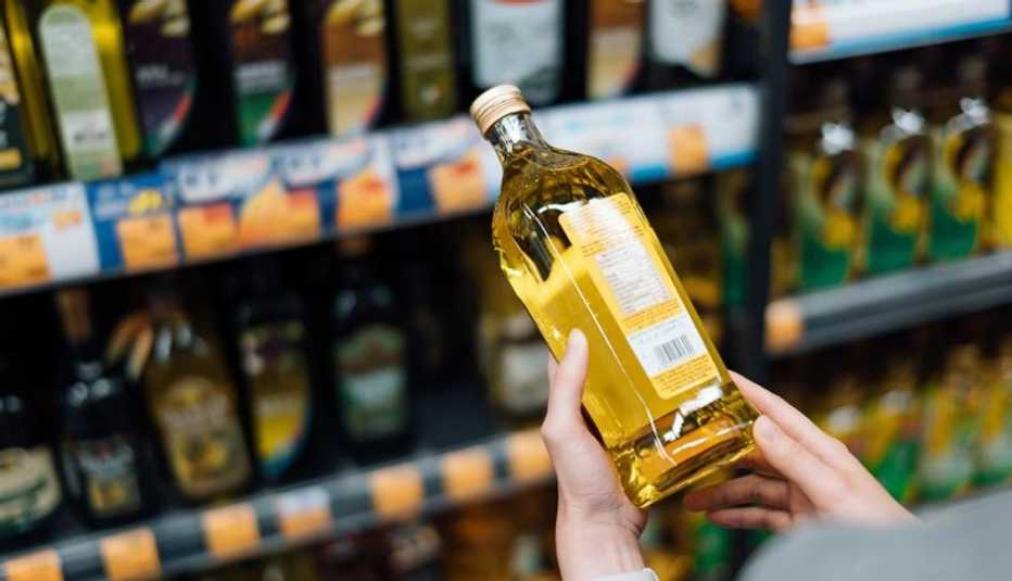 Una mujer revisa la etiqueta de una botella de aceite de oliva Una mujer revisa la etiqueta de una botella de aceite de oliva