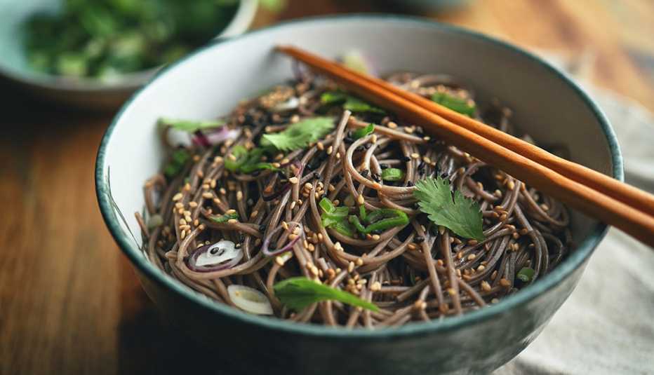 Palitos de comer sobre un bowl de fideos soba con sésamo, cilantro y salsa de soja