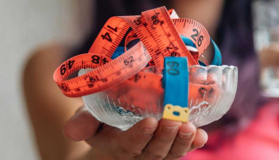 Mano de mujer que sostiene un pequeño envase de cristal con una cinta de medir