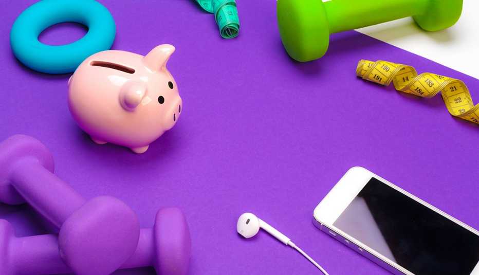 Alcancía en medio de un tapete de ejercicio, pesas livianas y un teléfono