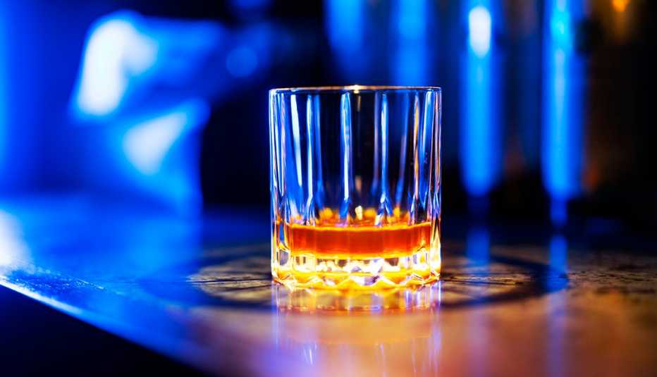 Un vaso con licor en un bar y una luz azul al fondo