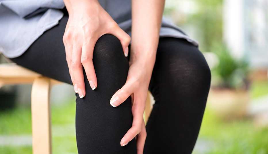 Una mujer se hace presión en la rodilla con sus manos