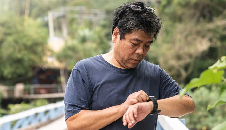 Un hombre mira el conteo de pasos en su reloj inteligente mientras camina por un sendero en el bosque