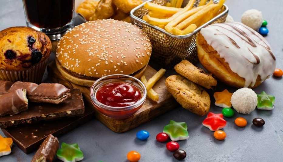 Variedad de alimentos procesados entre ellos chocolates, caramelos, una hamburguesa, donas, soda, galletas dulces y papas fritas