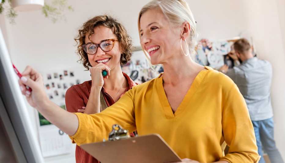 Dos mujeres sonriendo y mirando una pizarra